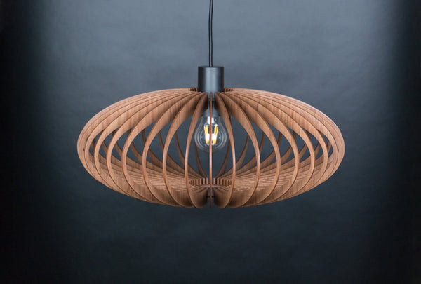Ellipse wooden pendant light – oval slatted shade, lit, hanging against a dark grey wall
