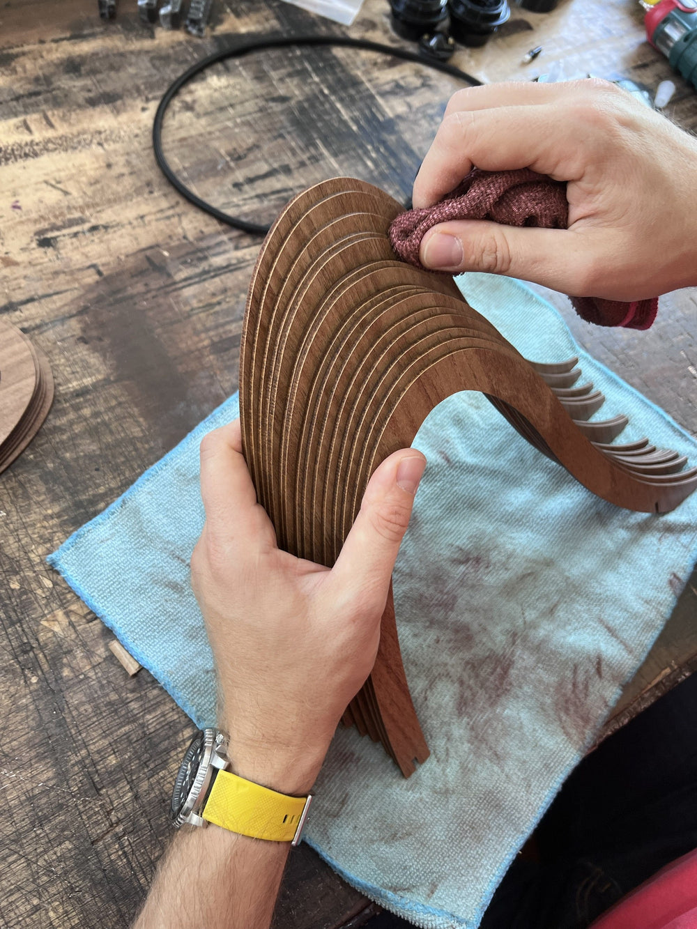 Martin's hands finishing a stack of laser-cut walnut-print HDF chandelier parts with a cloth